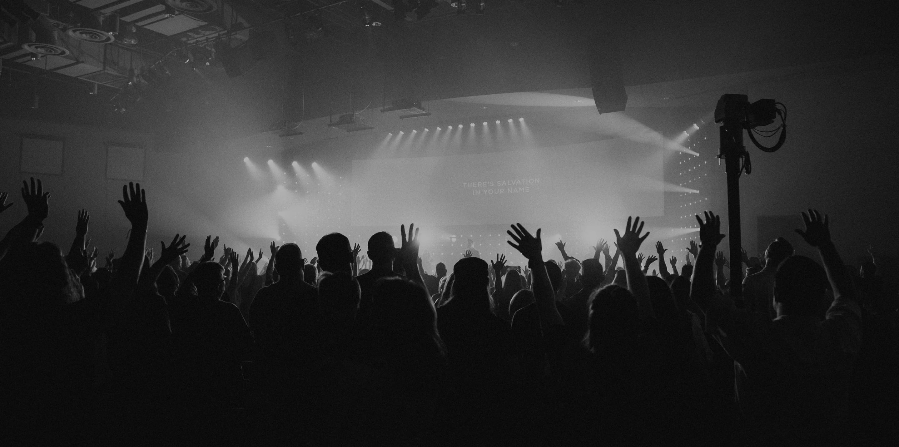 A large crowd looking at the stage at a concert in an arena, stylised in black and white